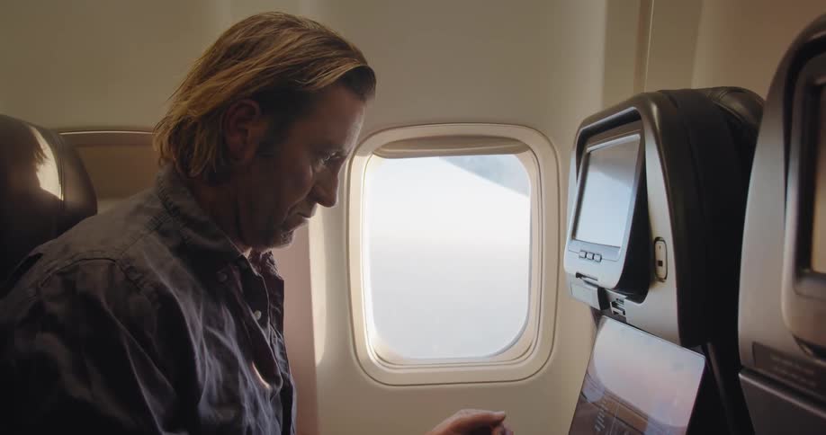 The man is typing on his laptop in the plane