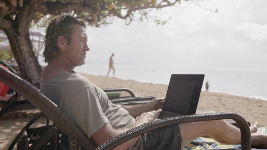 A man uses a laptop on the beach