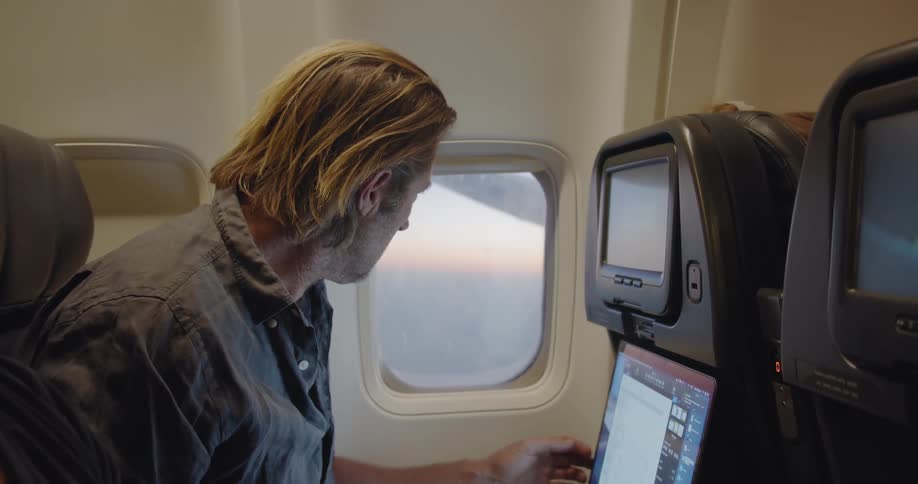 A man uses his laptop and looks out of the plane window