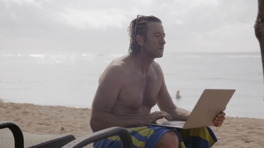 Man types on a laptop on a beach