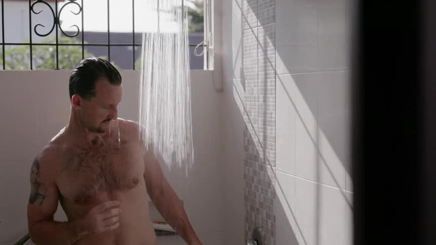 A man is finishing up taking a shower inside in daylight