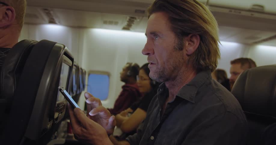 A man is using his phone on the plane