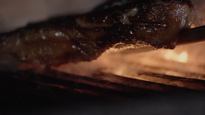 Person uses tongs to lift steak off grill