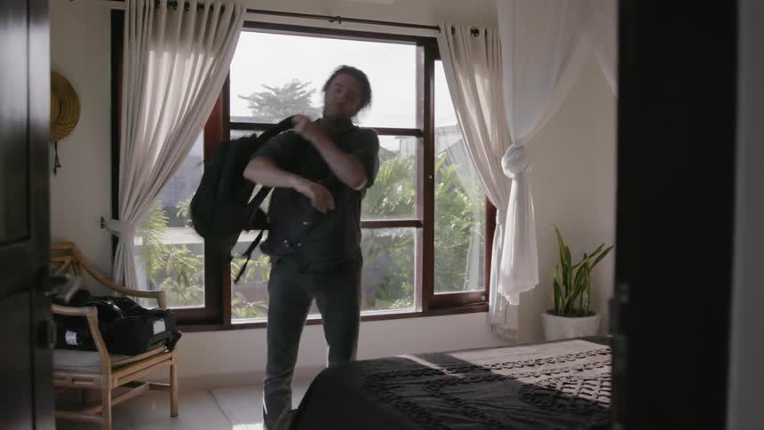 A man dresses himself and leaves a bedroom