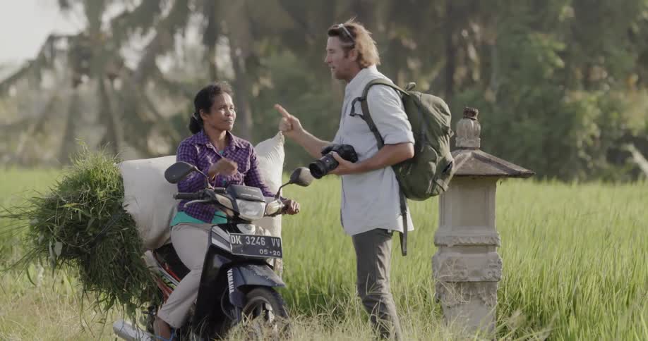 Man holding a camera shakes the hand of a woman sitting on a motorcycle