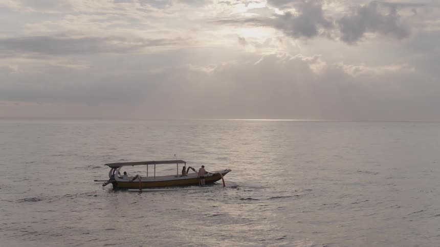 A man jumps off a boat into the ocean at sunset