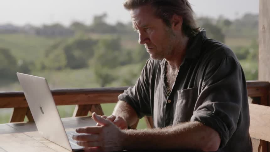 A man works on a laptop on a deck on a sunny day