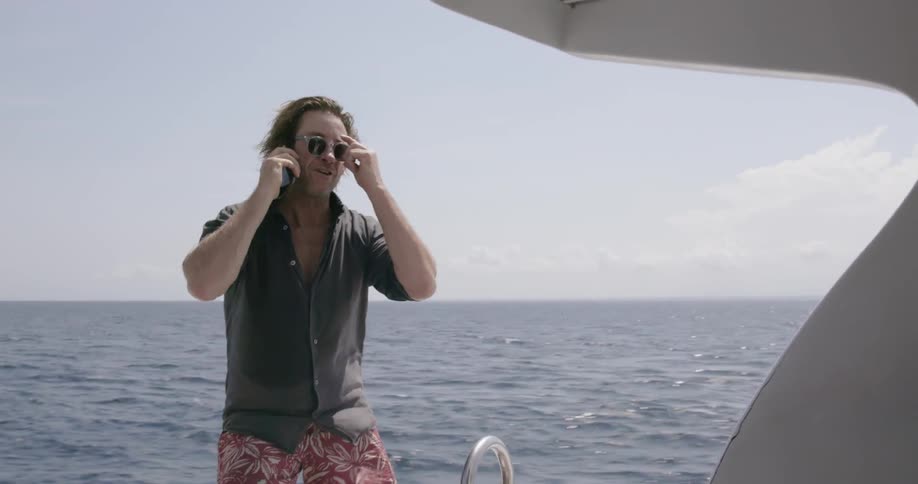 Man rides on a boat smiling and talking into a phone