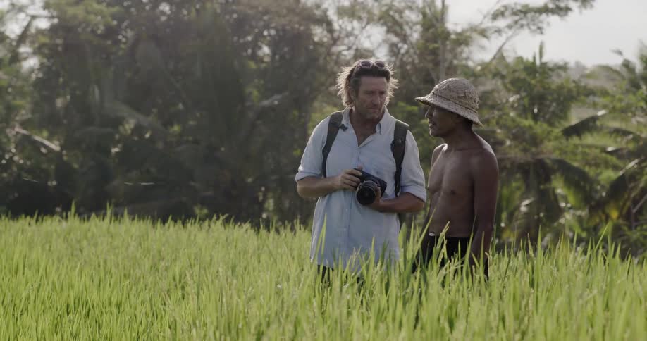 Two men standing in a field of tall grasses and one of them points