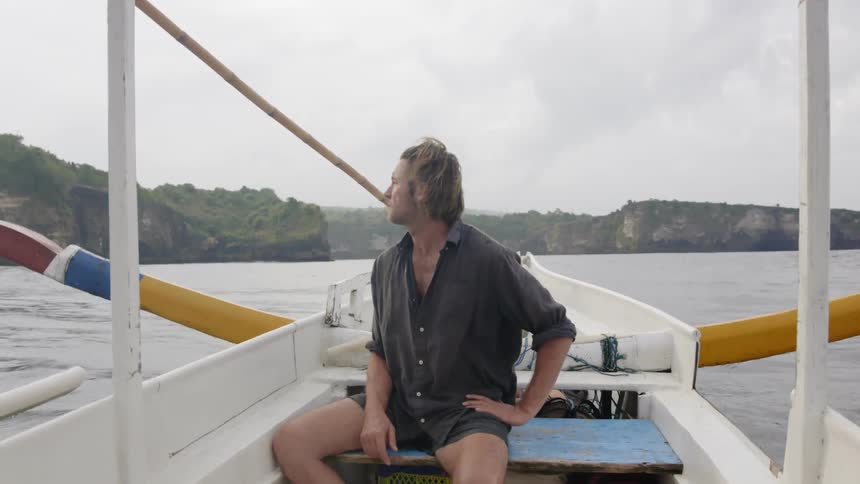 Man sits on a boat as it cruises across a lake