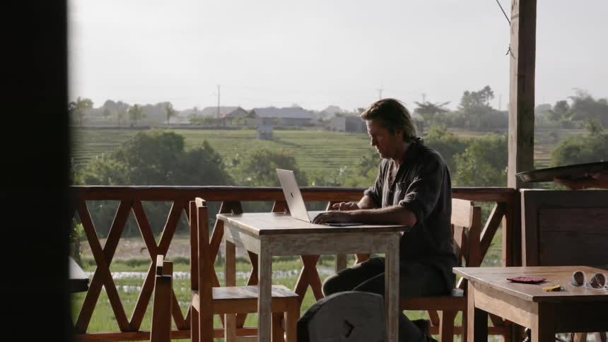 Man works on a laptop at a table as a waitress walks by