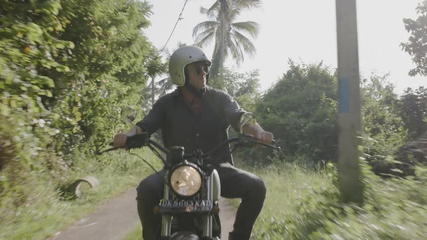 A man rides a motorcycle on a rural road on a sunny day