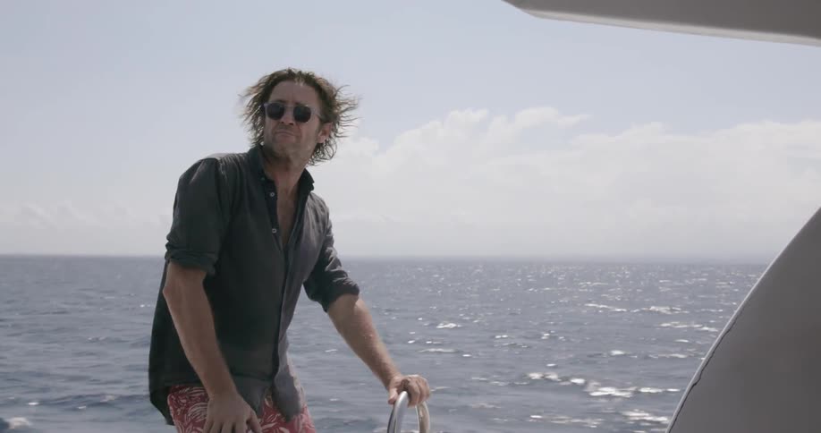 A man holds onto a rail as he stands on a moving boat