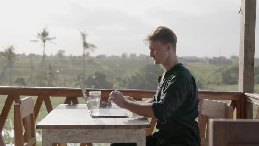 Man sits at a table outside as he works on a laptop