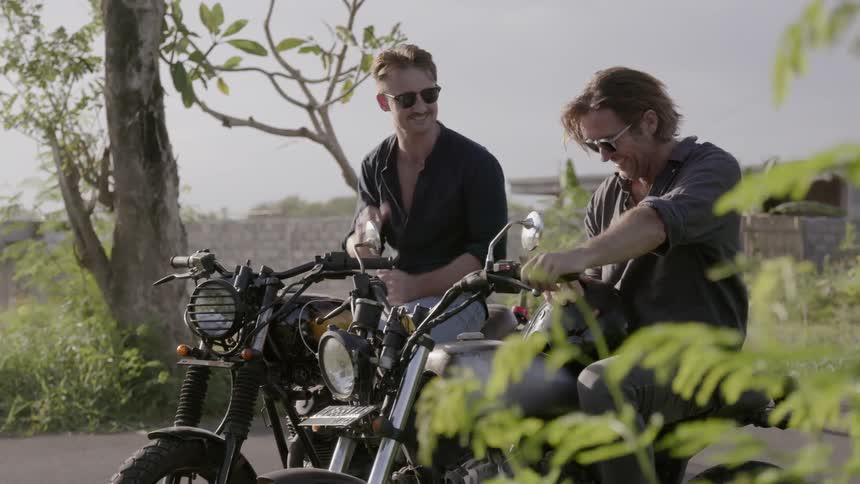Two motorcyclists talk while parked on the side of a road