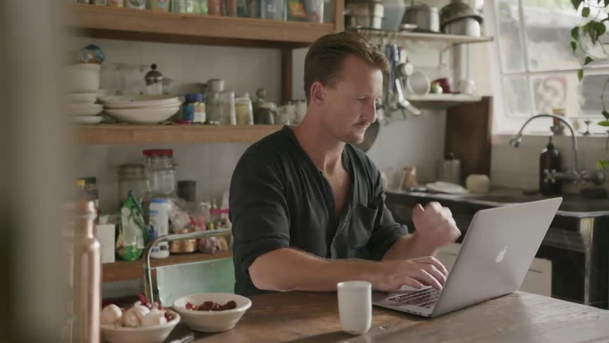 A man uses a laptop on a table in his kitchen