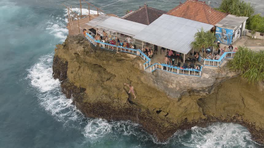 Person jumps off a cliff into the water by a house