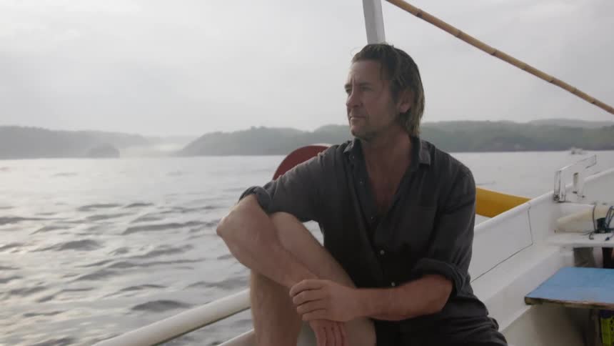 The man is leaning against the side of the moving boat