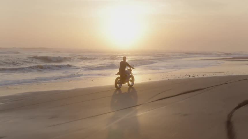 A motorcyclist rides on a beach at sunset