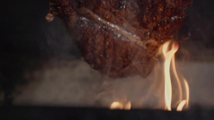 The steak is lifted from the flame of the grill