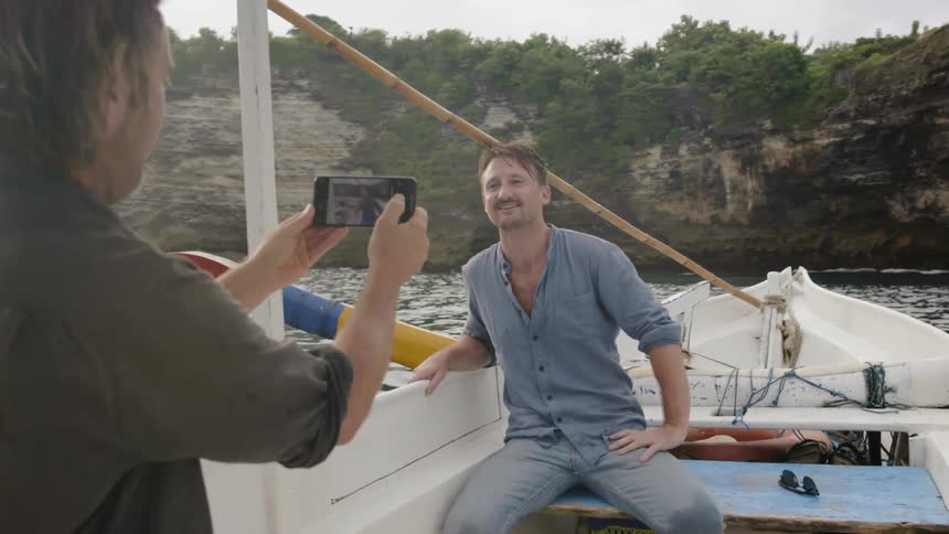 Man takes cell photo of another man riding on boat