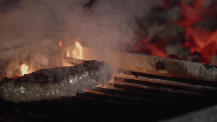 Flames flare up near the meat as it cooks on the grill