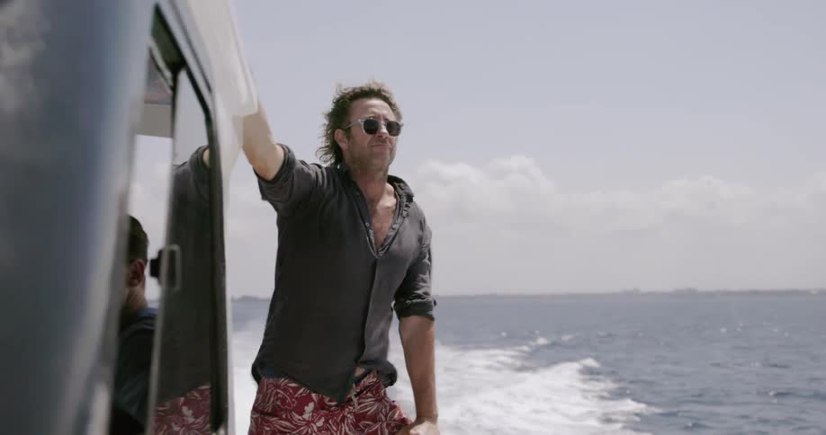 A man holds on to the side of a boat traveling in the ocean
