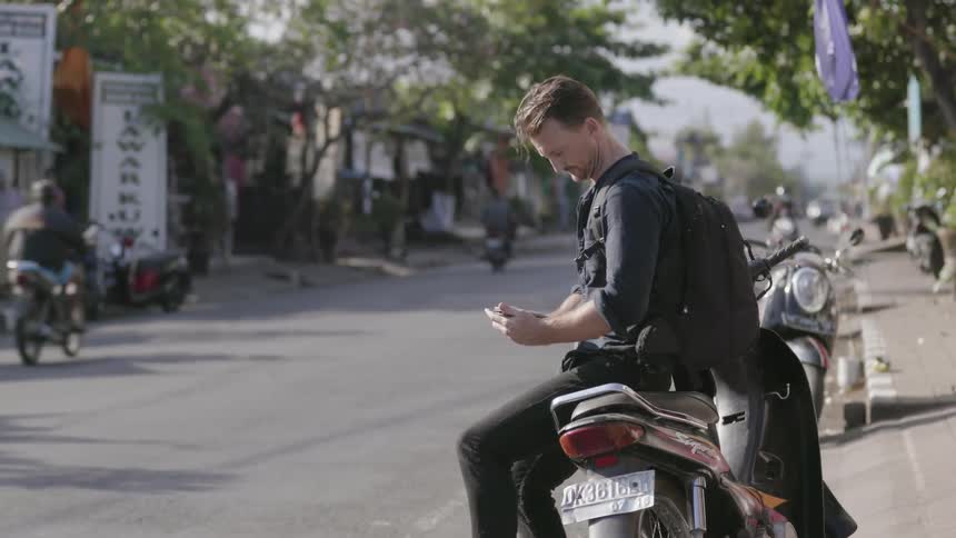 A man sits on a parked motorcycle on a city street