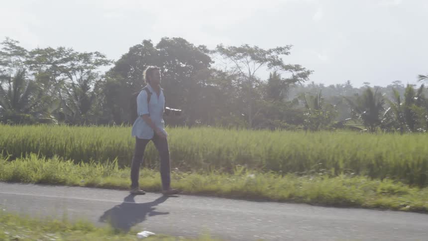 A man walks along the road holding a camera on a sunny day