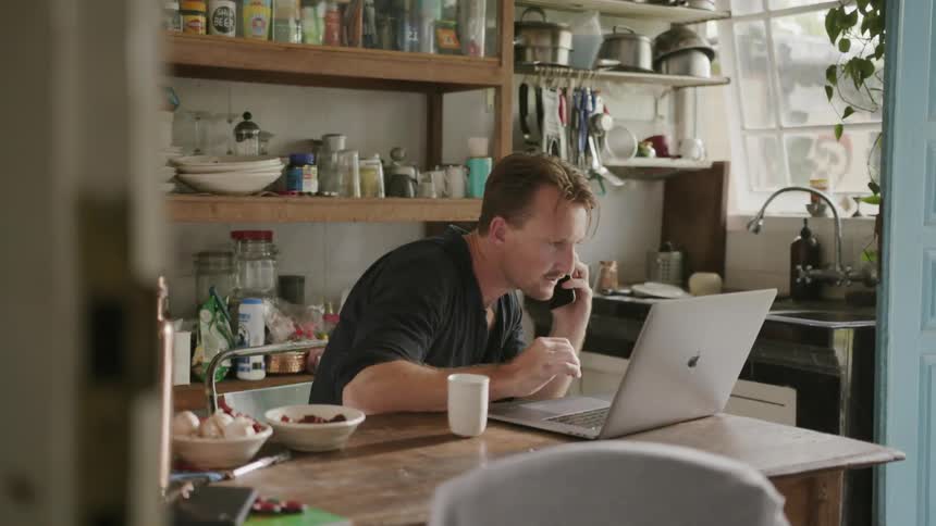 Man talks on a cellphone as he looks at a laptop