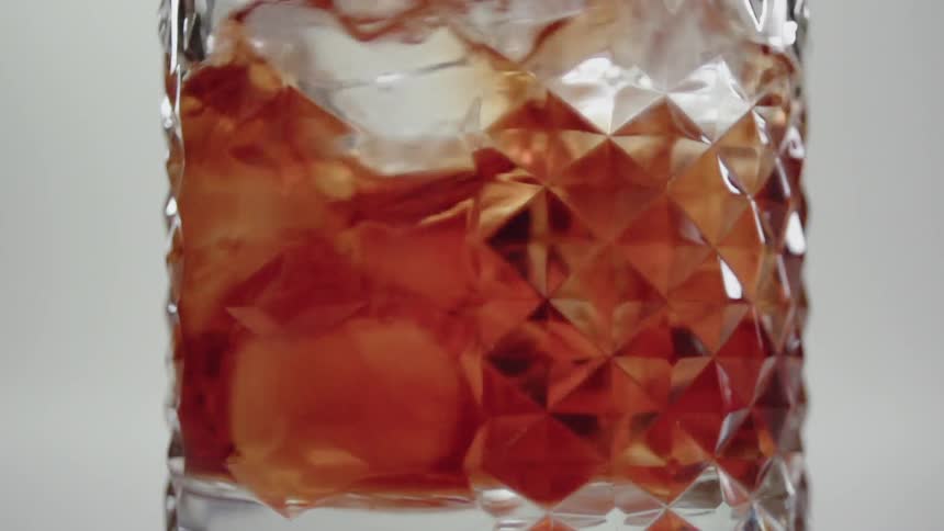 A cocktail is being stirred with ice in daylight