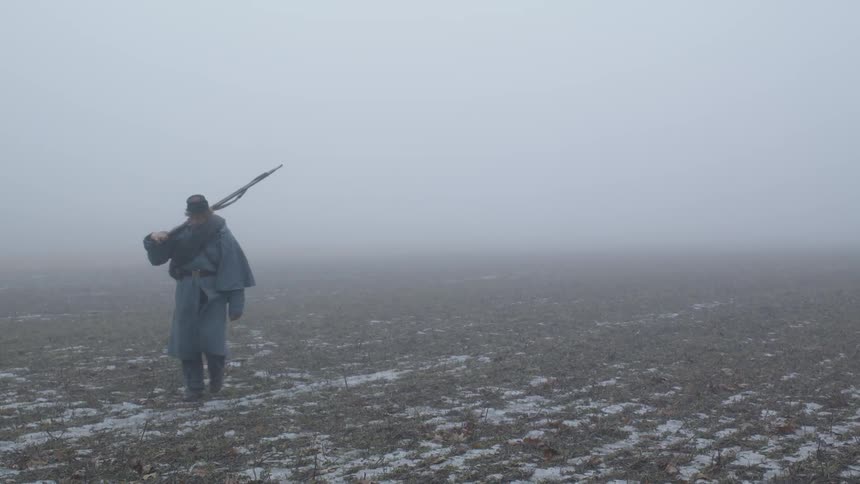 A solder carries a rifle across a foggy field