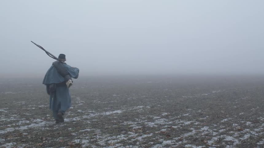 A soldier carries a rifle across a foggy field