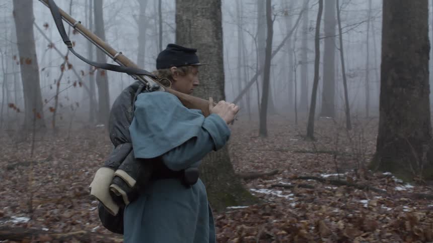 A soldier carries his rifle through the woods
