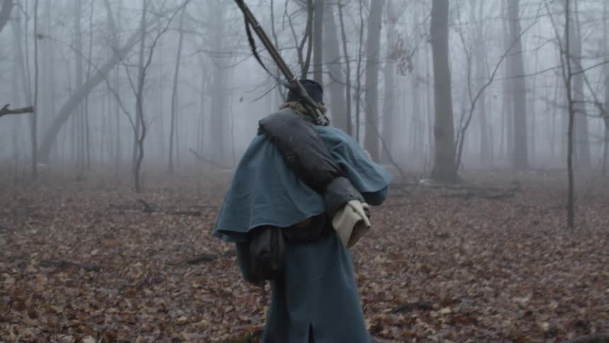 A soldier carries his rifle through the woods