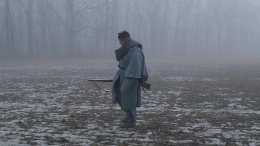 A soldier carries a rifle across a foggy field