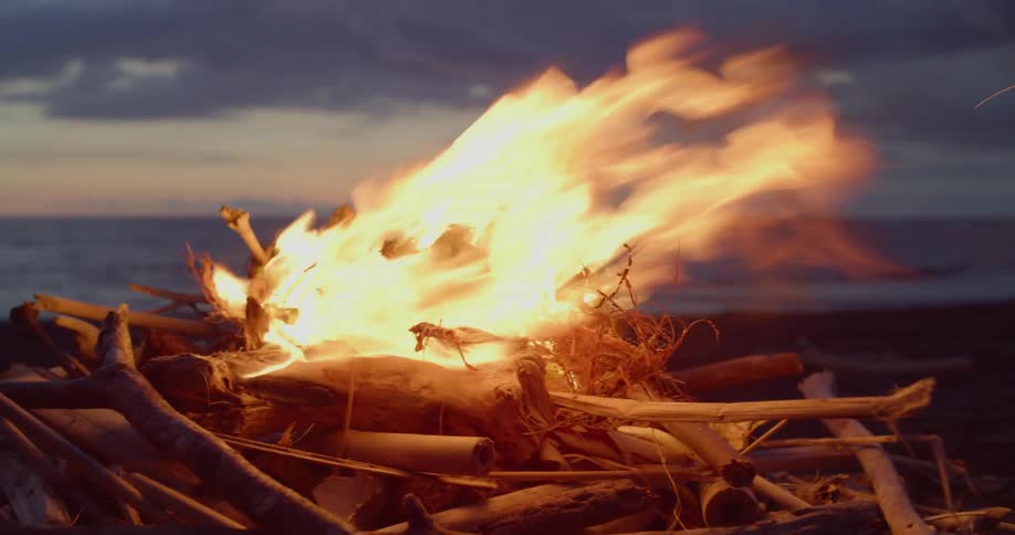 A bonfire burns on a beach at sunset