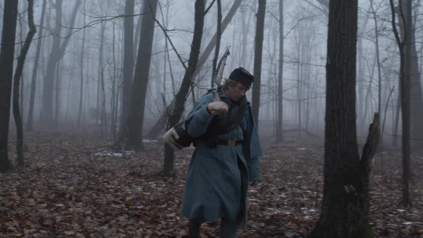 A soldier carries a rifle in foggy woods