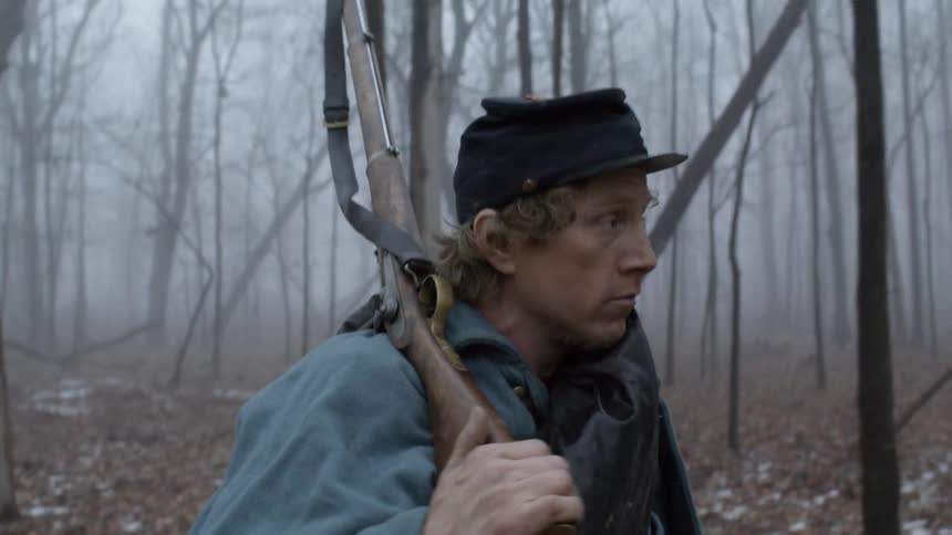 The man carries his rifle through the woods