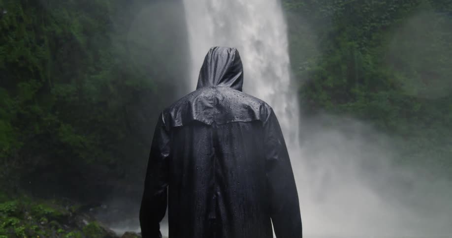 A man stands near the waterfall