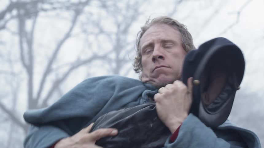 A civil war era soldier puts his pack on then replaces his cap