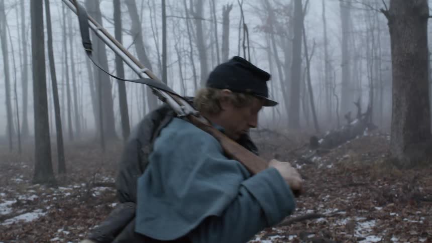 A soldier carries a rifle in a foggy forest
