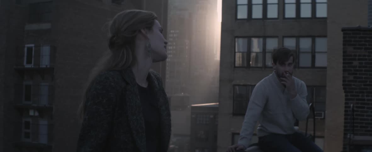 A man and woman sit on a rooftop in the city