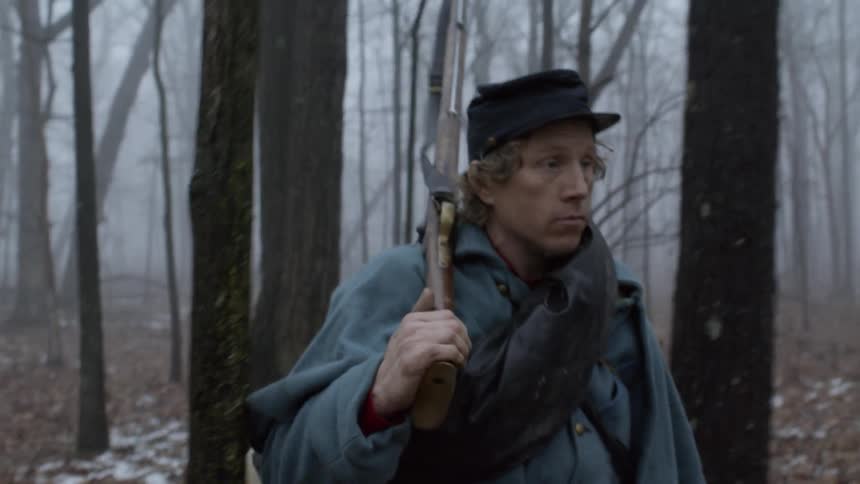 A soldier walks through the woods carrying his rifle on his shoulder