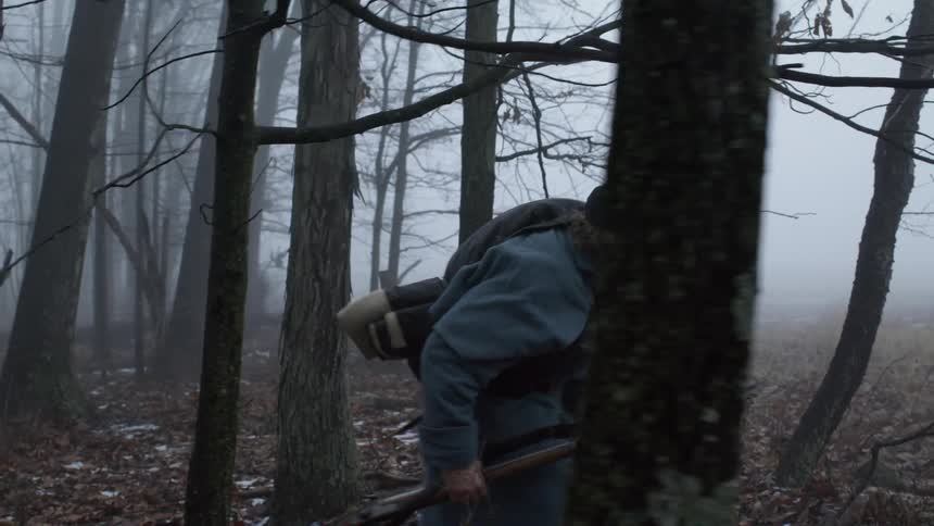 A soldier is carrying his rifle as he walks through a forest on a foggy morning
