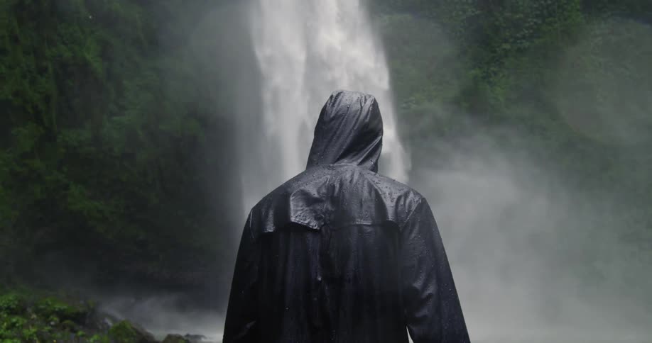 Person in rain jacket approaches waterfall