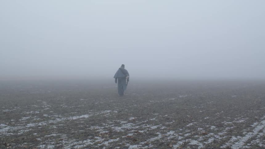 A man walks across a foggy field