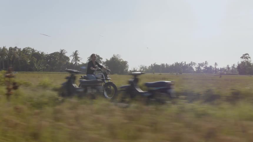 Man rides a motorcycle on a path through a grassy field