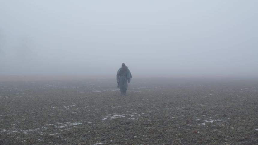 Man walks through a large field on a foggy day