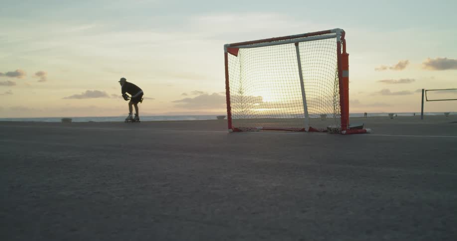 A man plays roller hockey on a beach at sunset